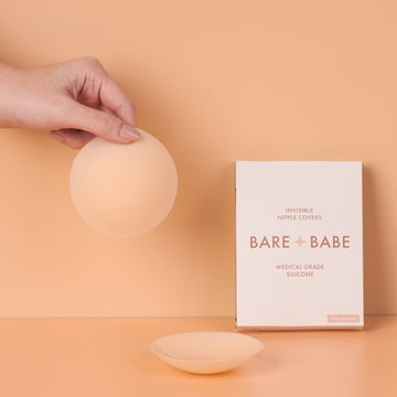 Hand holding a Bare Babe Non-Adhesive Nipple Cover beside its box, with a second cover on the table, reusable silicone nipple covers you can wear 100+ times