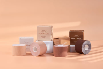 Boob Tape Kit: four rolls of breast lift tape in four of the five shades, Creme through Mocha, in front of their boxes, the tape used to lift and shape under a strapless dress.